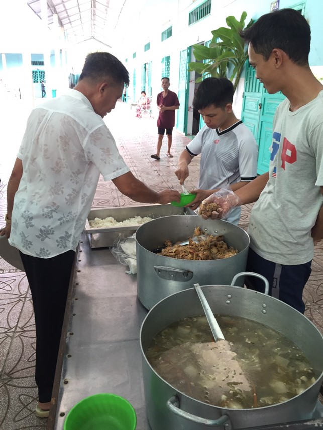 A group of people standing next to large metal pots of foodDescription automatically generated